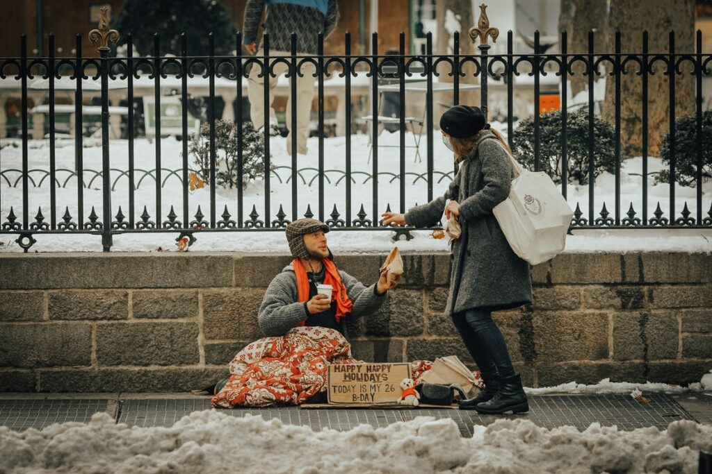 A woman making a donation to a man on the street during the holiday season