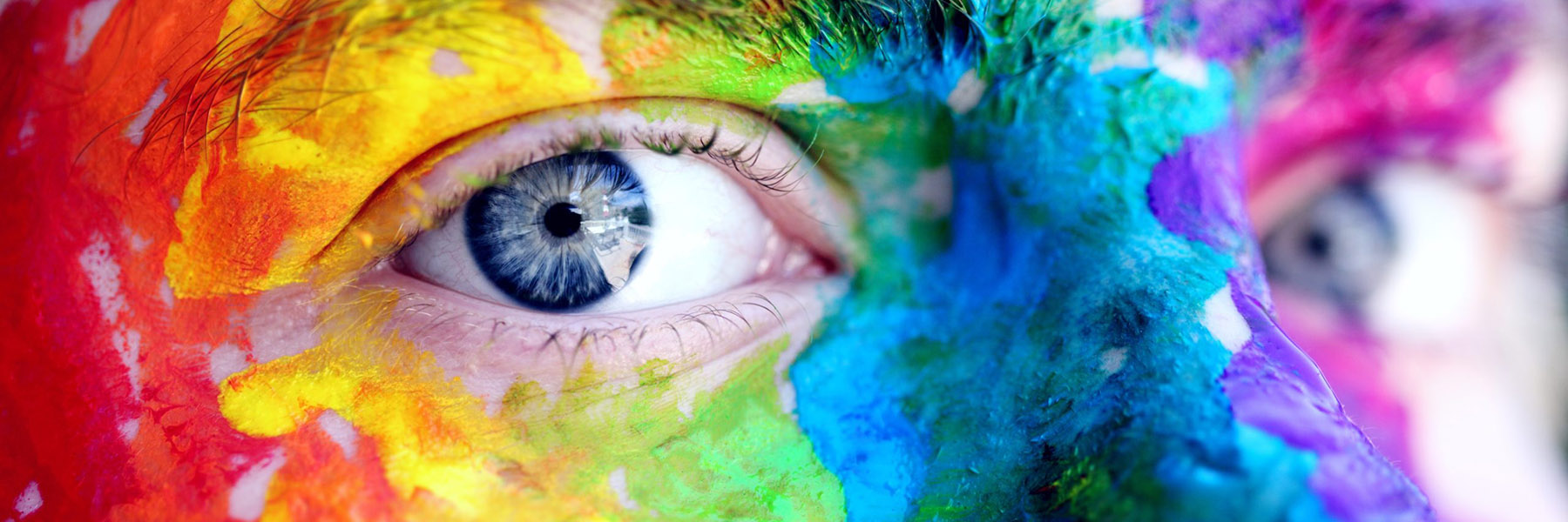 blue-eyed person with rainbow colours painted on their face