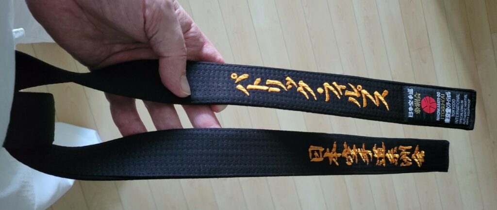 This image shows the Phillips's black belt. 'Patrick Phillips' in Japanese (displayed top of the image). the name of the Japanese Karate Organization (bottom of the image)