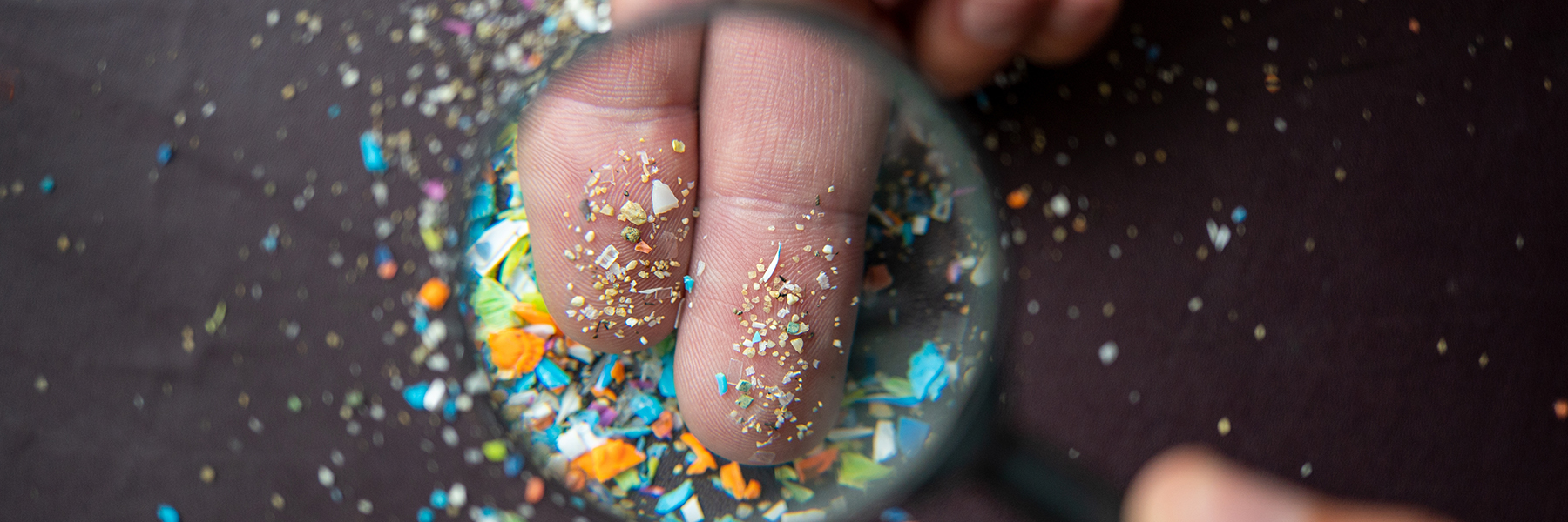 Close-up of micro plastic particles on the fingers under a magnifying glass. Concept for water pollution and global warming. Macro shot on a bunch of microplastics that cannot be recycled