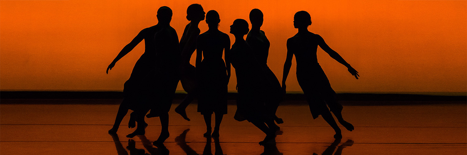 Figures dancing on stage in silhouette against sunset-coloured background
