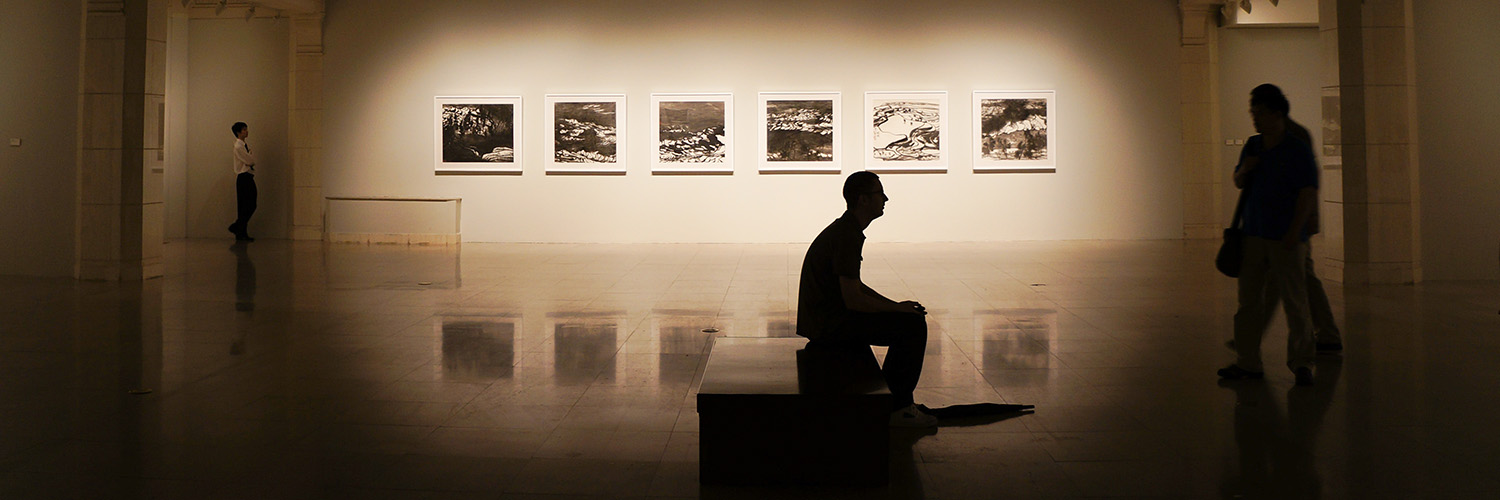 Man's silhouette sitting in front of illuminated art gallery exhibit in the background, stock banner image from pexels