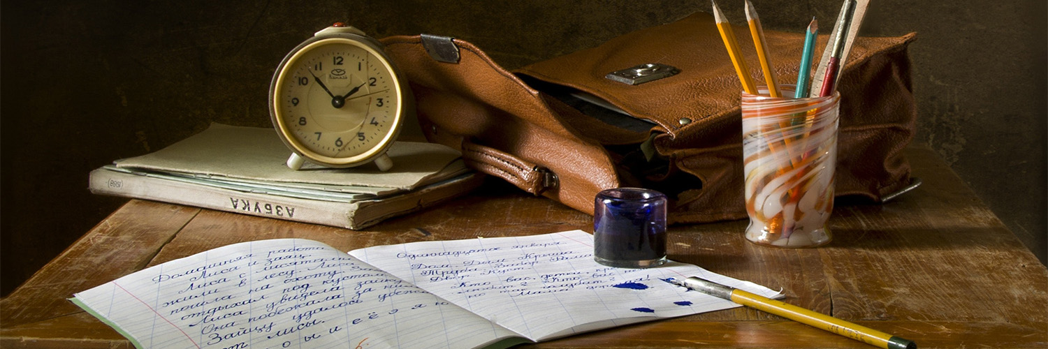 Wooden desk covered in books, writing implements and an old-timey alarm clock