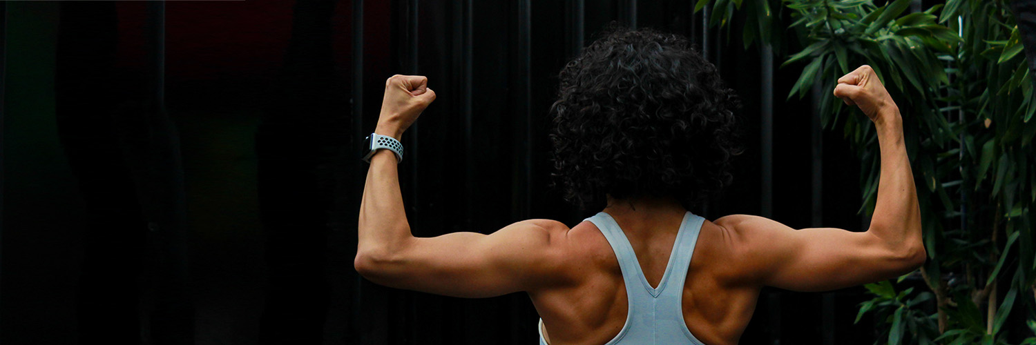 Woman with back turned to camera flexing arms and shoulders in front of black background