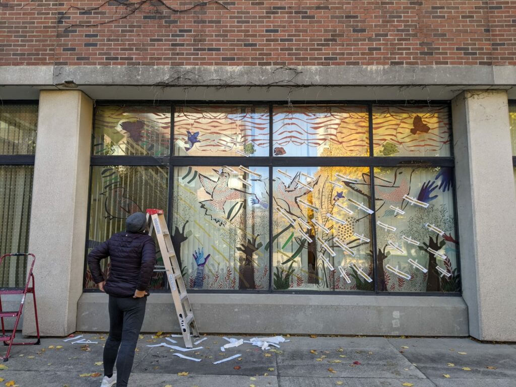 York University student looking at art mural she just installed on a window
