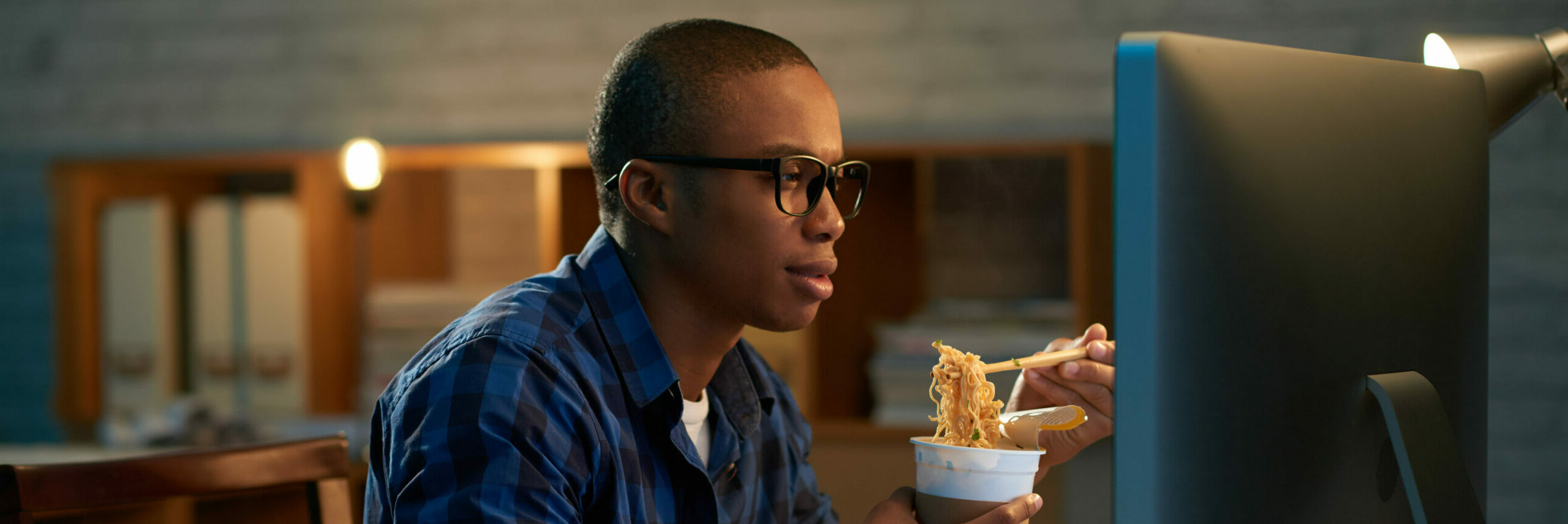 Black man eating noodles while working at computer