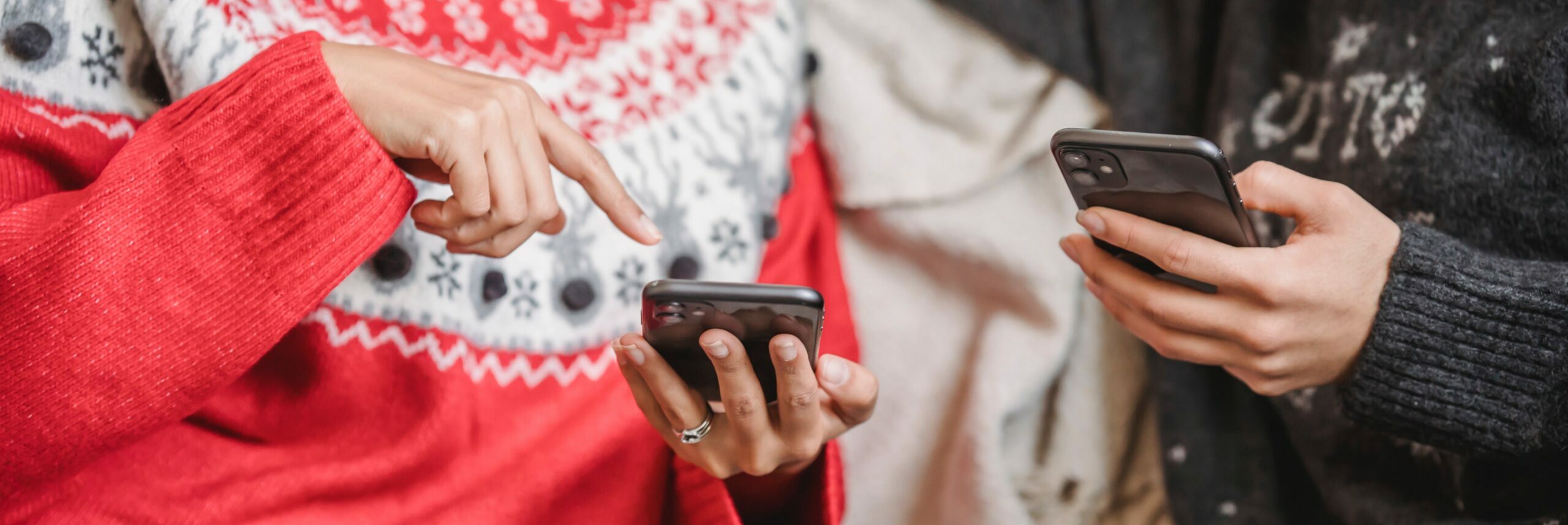 Two people wearing holiday-themed sweaters on smart phones